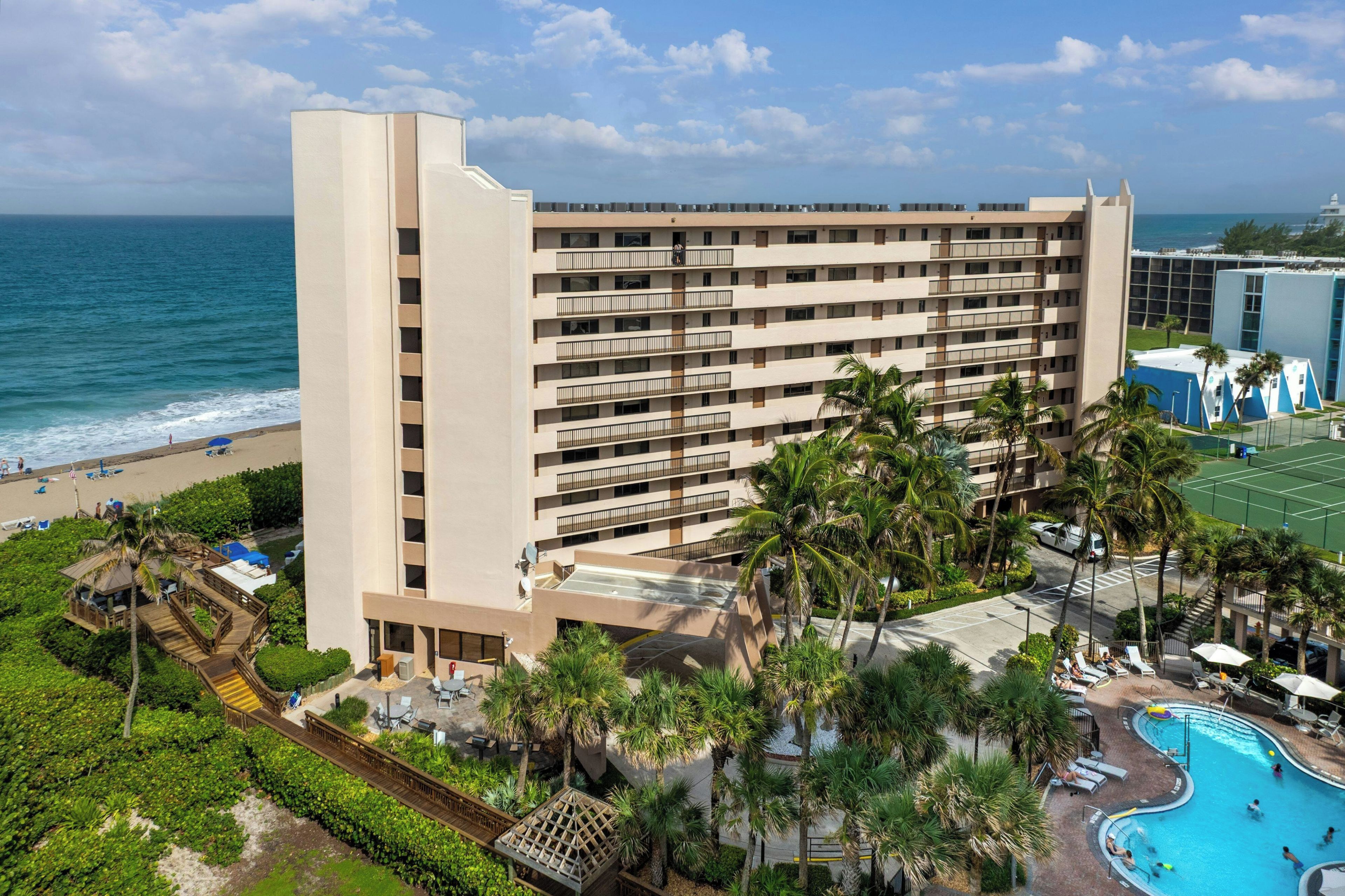 A multi-story hotel with a pool, beach access, and palm trees.