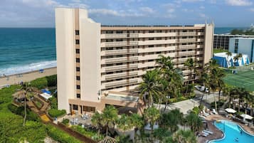 A multi-story hotel with a pool, beach access, and palm trees.