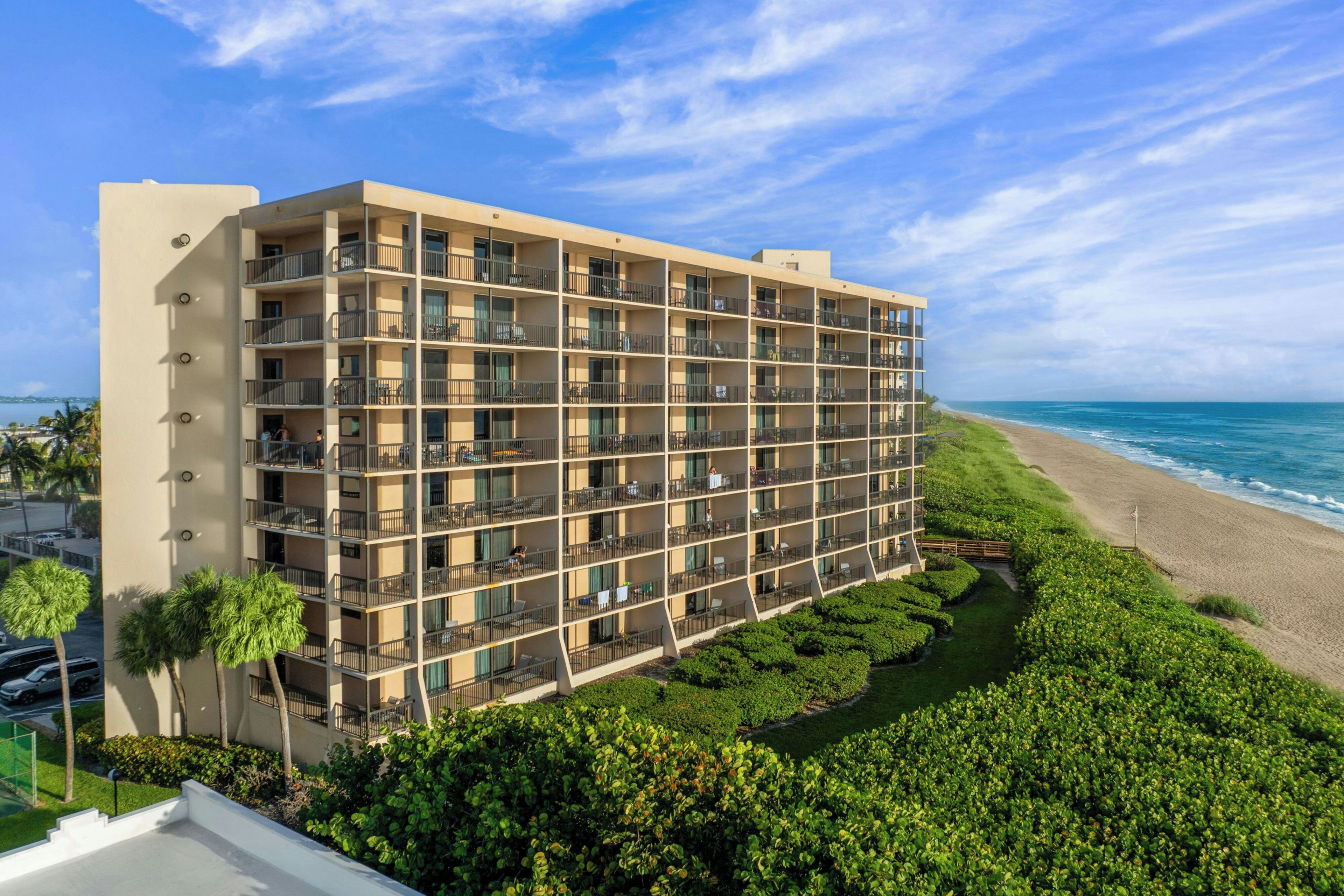 A multi-story hotel with balconies, located near a beach.