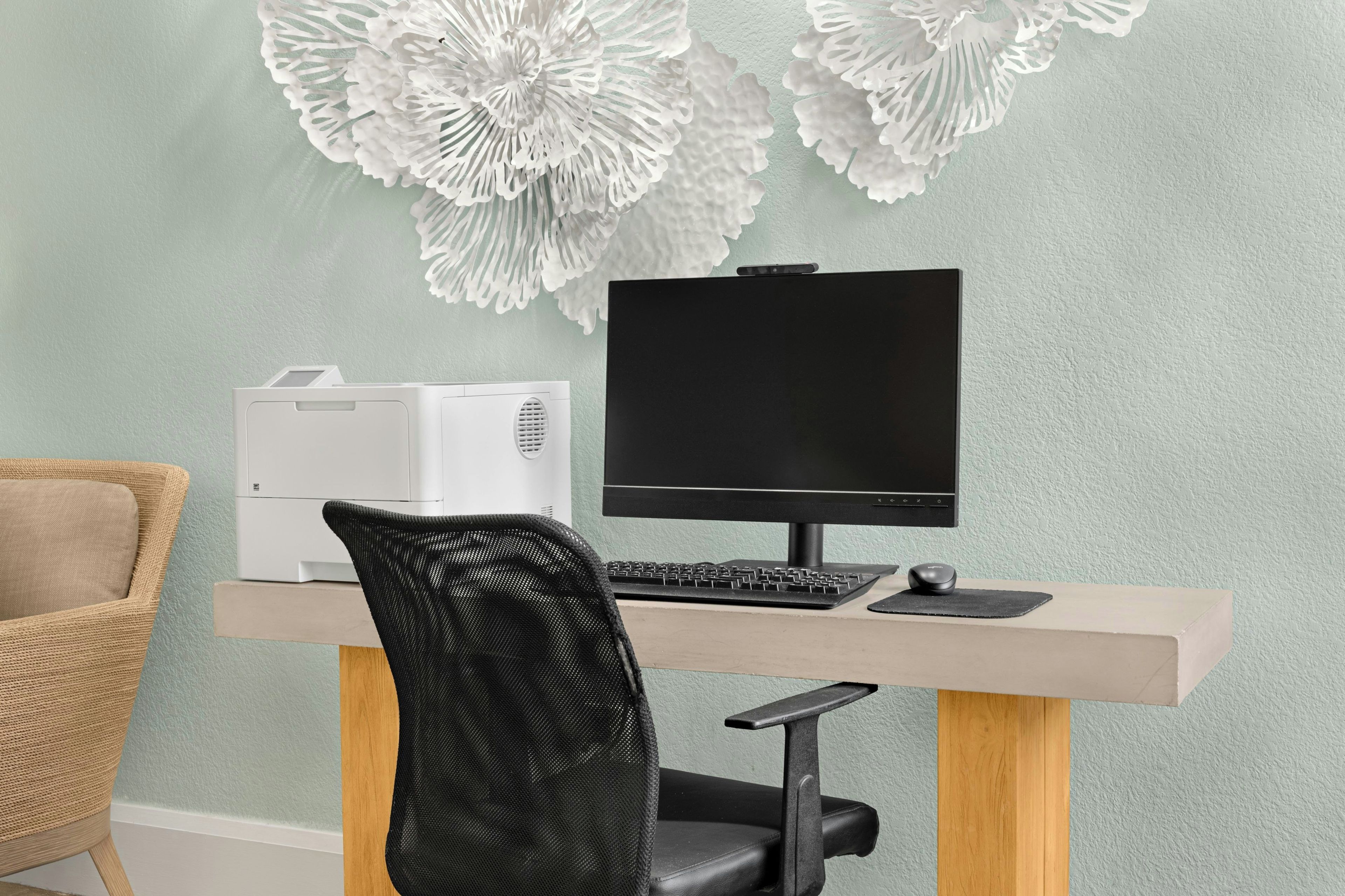 A home office setup with a computer, keyboard, and mouse on a desk, a printer, a chair, and decorative wall art.