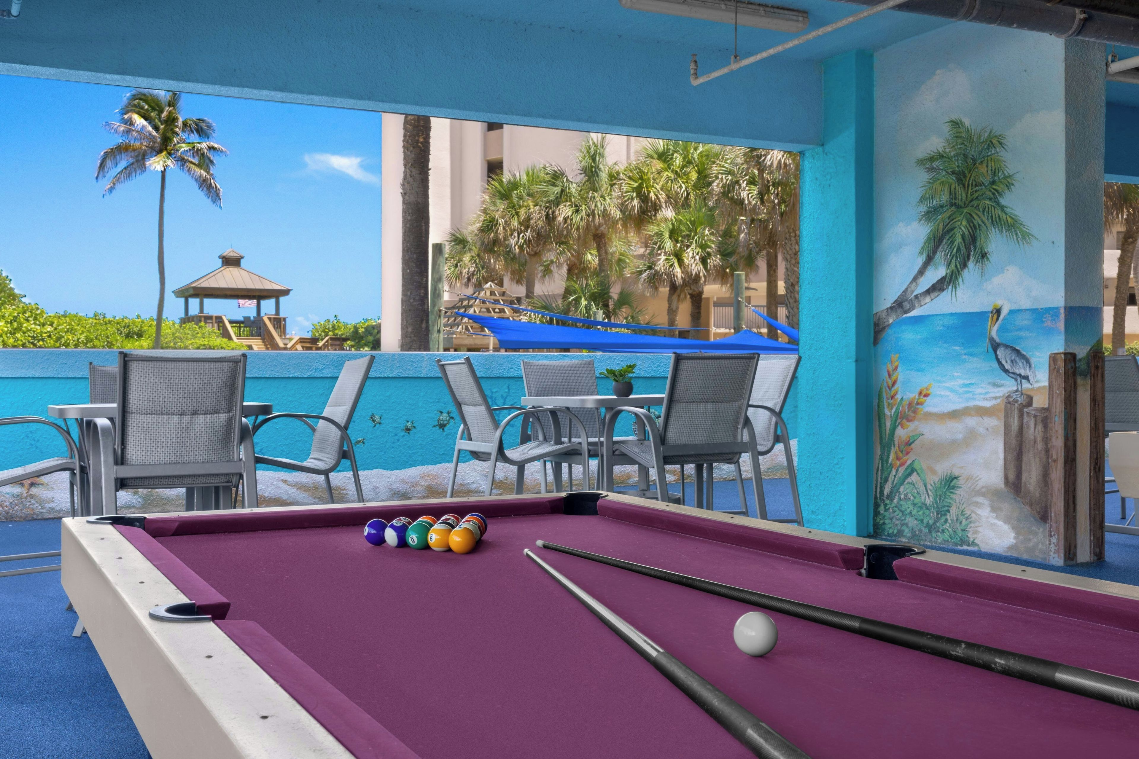 A pool table with balls, chairs, and a mural of a beach scene.