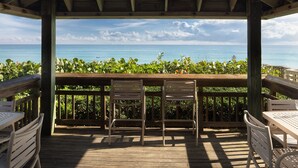 A wooden deck with two metal chairs and a table, overlooking a lush garden and the ocean. - Vistana Beach Club (Jensen Beach)