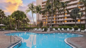 A hotel pool area with a clear sky, palm trees, and a multi-story building in the background.