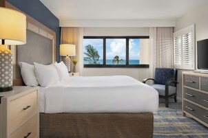 Une chambre d’hôtel avec un grand lit, un bureau, une chaise, une télévision et une fenêtre donnant sur la mer.