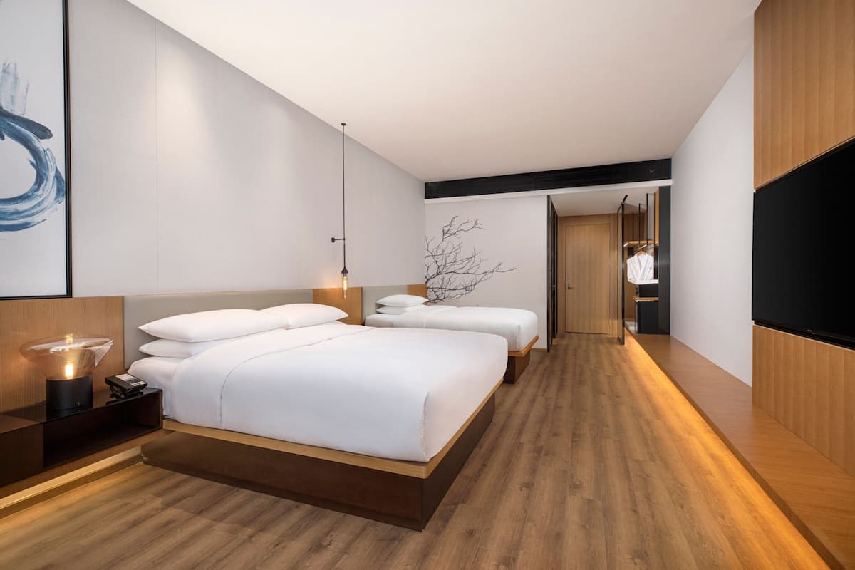 A modern hotel room with a large bed, bedside tables, a TV, and a wooden floor.