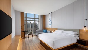 Ein modernes Hotelzimmer mit einem großen Bett, einem Schreibtisch, einem Stuhl und einem Fernseher.