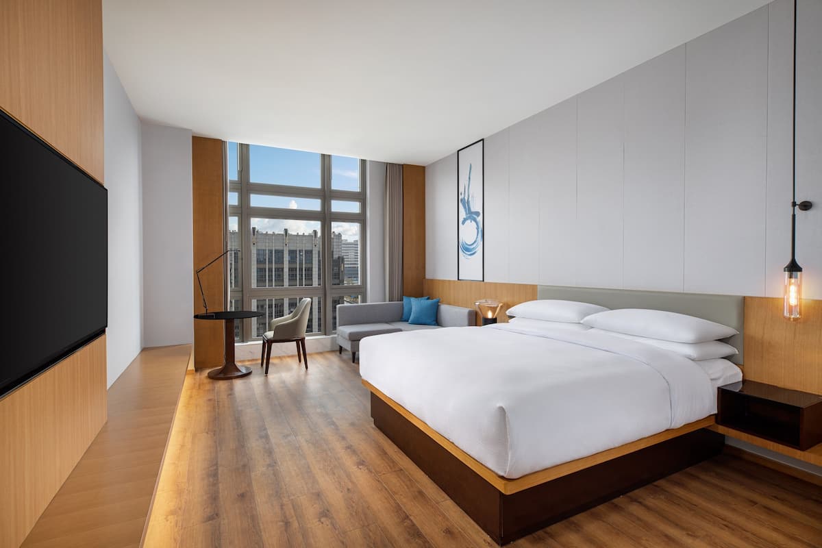 A modern hotel room with a large bed, a desk, a chair, and a TV.
