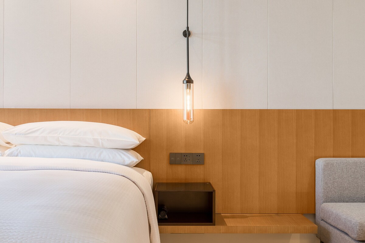 A modern bedroom with a wooden headboard, a bedside table, and a grey sofa.