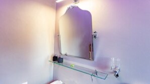 A bathroom with a mirror, a shelf with toiletries, and a light fixture. - Jade Park (Giovinazzo)