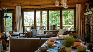 Een gezellig chaletinterieur met een houten eettafel gedekt voor een maaltijd, een comfortabele zithoek met een bank en stoelen, en grote ramen met uitzicht op het omliggende bos.