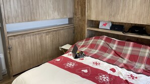 Ein Schlafzimmer mit Holzwandverkleidung, einem Bett mit rot-weiß kariertem Überwurf und einem Regal mit Taschen und einem Laptop.