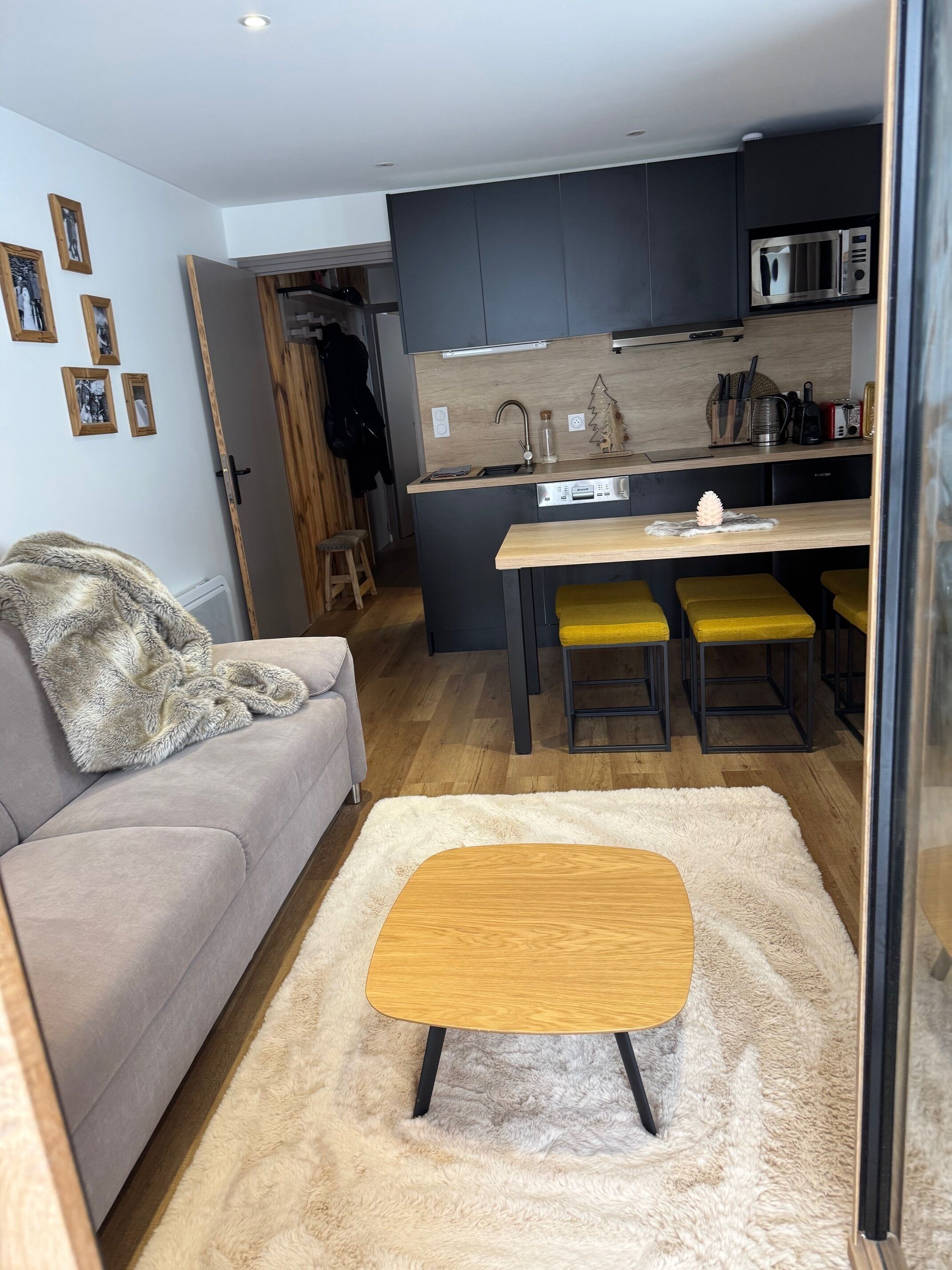 Un espace de vie compact comprenant un coin cuisine, un canapé, une table basse et un petit coin repas avec des tabourets jaunes.
