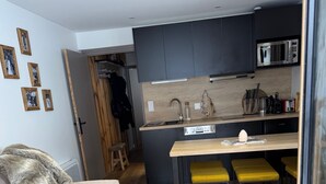 Ein kompakter Wohnbereich mit Küchenzeile, einer Couch, einem Couchtisch und einer kleinen Essecke mit gelben Hocker.