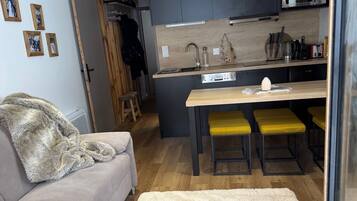 Un espace de vie compact comprenant un coin cuisine, un canapé, une table basse et un petit coin repas avec des tabourets jaunes.