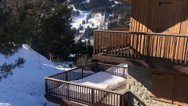 Eine Holzhütte mit einem Balkon mit Blick auf eine verschneite Berglandschaft.
