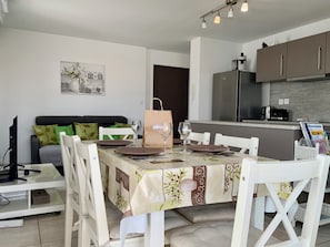 A dining area with a table set for four, a sofa, a kitchen with modern appliances, and a wall-mounted artwork.