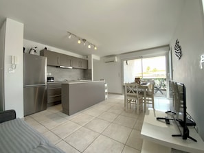 A modern kitchen with a central island, a dining area with a table and chairs, and a TV on a stand.