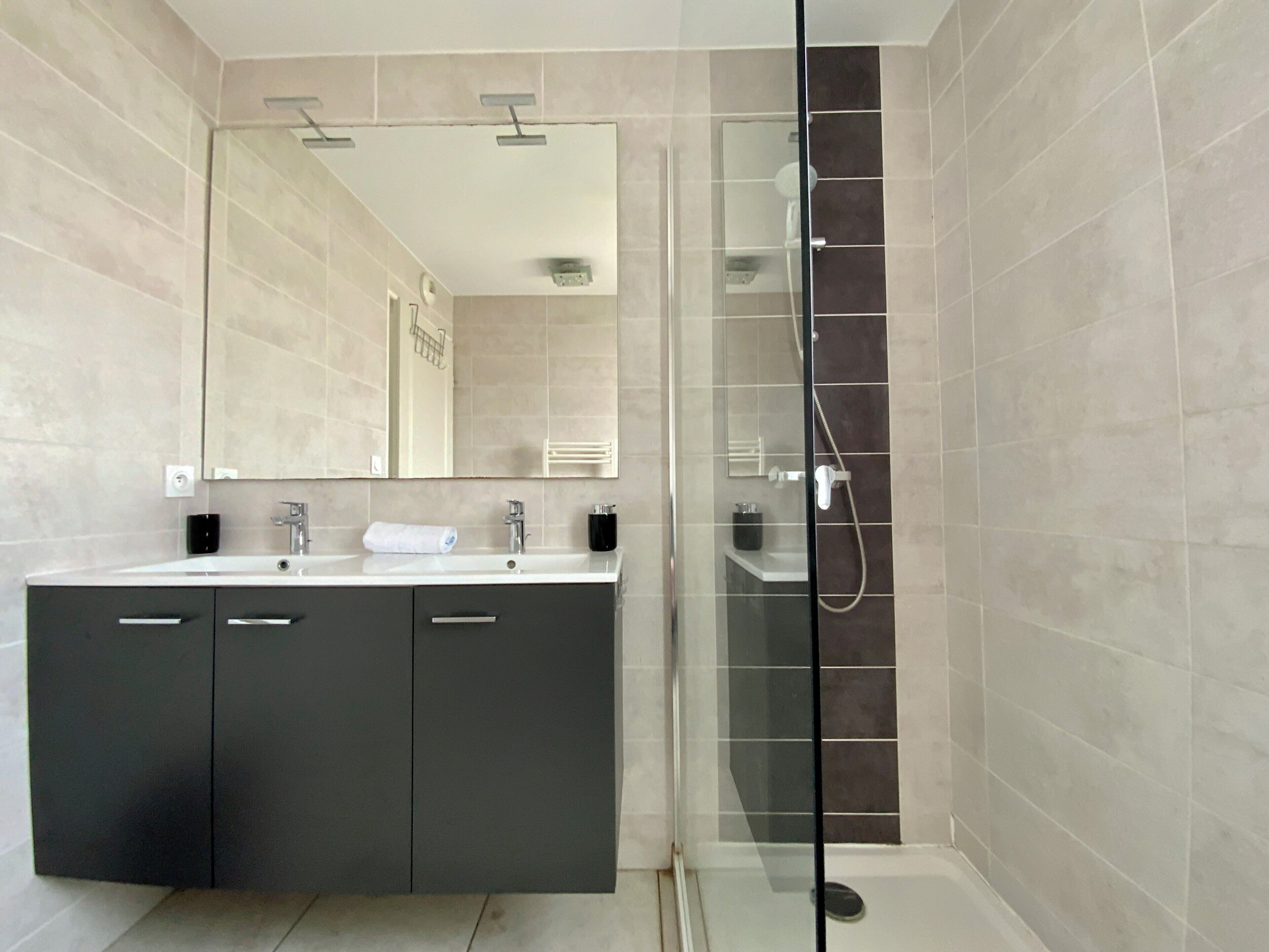 Une salle de bain moderne dotée d’une douche à parois de verre, d’un grand miroir et d’un meuble-lavabo à deux vasques.
