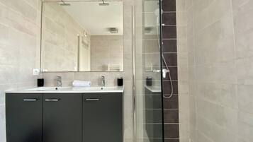 Une salle de bain moderne dotée d’une douche à parois de verre, d’un grand miroir et d’un meuble-lavabo à deux vasques.