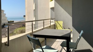 A balcony with a table and chairs, overlooking a beach and other buildings.