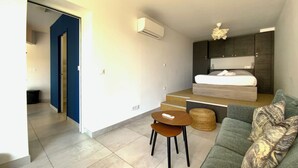 A modern, compact living space with a bed, a sofa, a small table, and a staircase leading to an upper level.