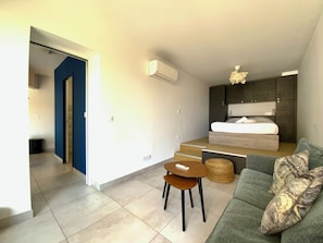 A modern, compact living space with a bed, a sofa, a small table, and a staircase leading to an upper level. - Rêve bleu appartement vue mer B203 dans résidence avec accès plage privé (Le Grau-du-Roi)