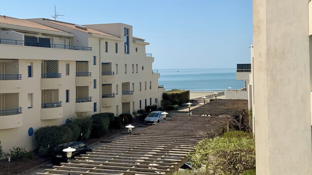 A multi-story building with balconies, a parking area, and a view of the sea.