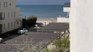 A coastal view with a building, a parked car, and a beach in the background.