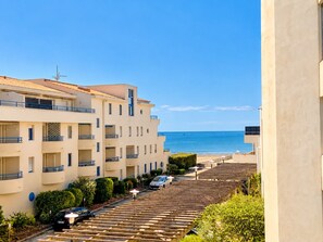 A coastal residential area with multi-story buildings, a parking area, and a view of the sea.
