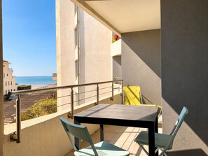 A balcony with a table and chairs, overlooking a beach and other buildings.