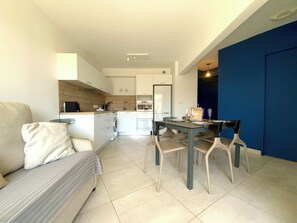 Un soggiorno moderno con un divano, un tavolo da pranzo con sedie, un angolo cottura con elettrodomestici e una parete decorata in blu.