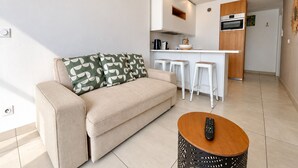Un salon moderne avec un canapé, une table basse et un coin cuisine équipé d’un tabouret de bar.