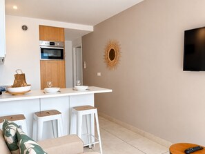 A modern kitchen with a built-in oven and microwave, a white countertop, and a wall-mounted TV. - Terrasse ensoleillée : appartement 1 chambre 1 cabine vue mer terrasse (Le Grau-du-Roi)