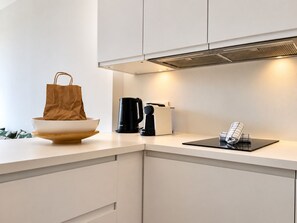 A modern kitchen with white cabinetry, a black coffee maker, a white kettle, and a brown paper bag on the counter. - Terrasse ensoleillée : appartement 1 chambre 1 cabine vue mer terrasse (Le Grau-du-Roi)