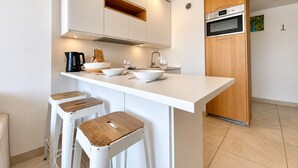 Une cuisine moderne avec des meubles blancs, un îlot central doté de tabourets et des appareils électroménagers intégrés.