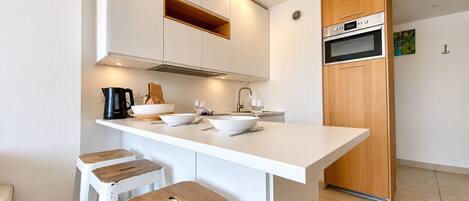 A modern kitchen with white cabinetry, a central island with stools, and built-in appliances.