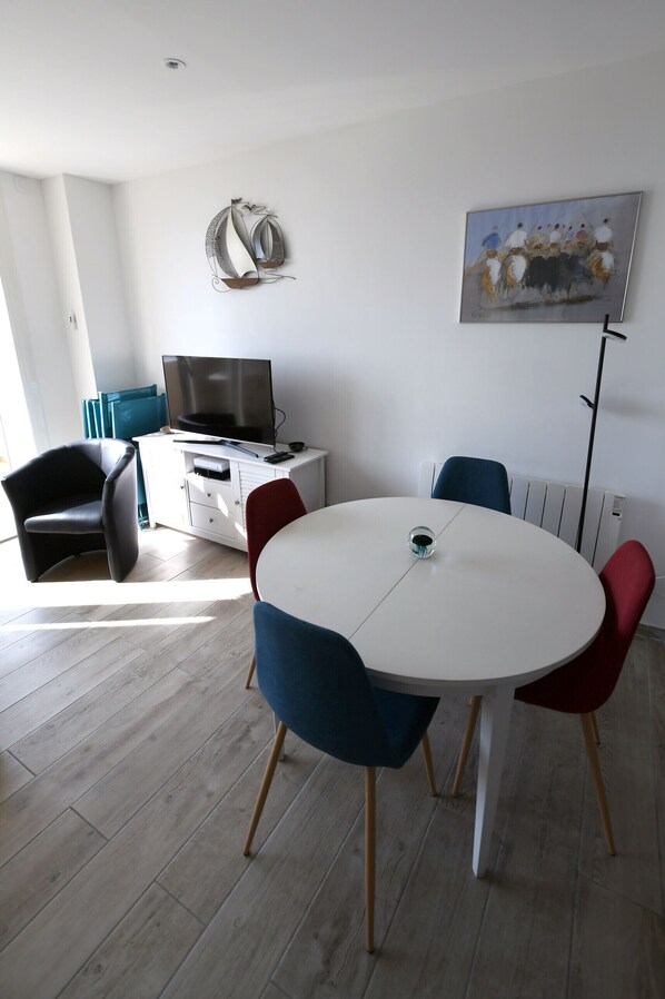 A modern living room with a round table, a flat-screen TV, a sofa, and a painting on the wall.