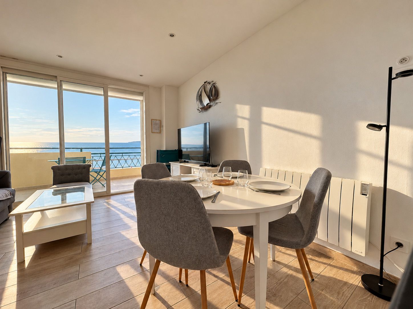 A modern dining area with a view of the sea, a flat-screen TV, and a balcony with outdoor furniture.