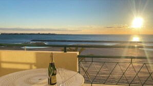 A balcony with a table set for two, overlooking a beach and the ocean.