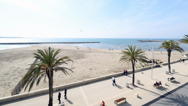 A beach with palm trees, a promenade, and a lighthouse in the distance.
