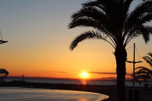 A sunset over a beach with a palm tree in the foreground.