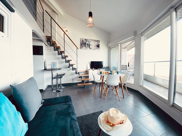 A modern living space with a staircase, a dining area, and large windows.