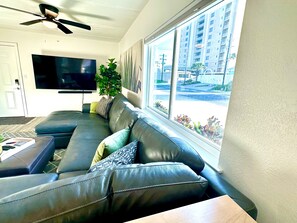 Een moderne woonkamer met een leren bank, een flatscreen-tv, een plafondventilator en een groot raam met uitzicht op de stad.