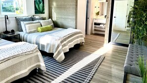 Un dormitorio moderno con una cama grande, mesitas de noche, un banco y vistas al baño.