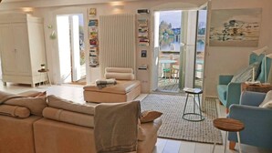 Una sala de estar moderna con un sofá, sillones y una mesa de centro. Se ve una estantería con libros y un cuadro en la pared.