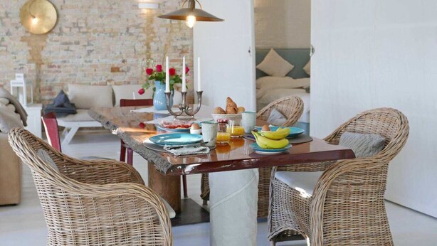 Un comedor con sillas de mimbre, una mesa de madera y una pared de ladrillo.