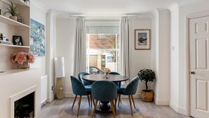 Un coin repas avec une table ronde, quatre chaises, une plante en pot et une vue sur la rue par une fenêtre.