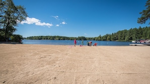 A sandy beach with a lake, trees, and a clear sky.