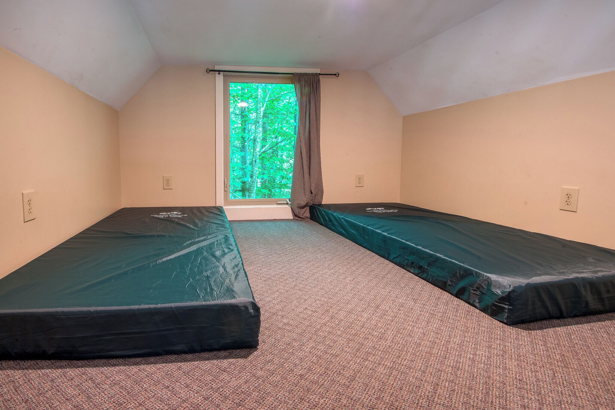 A small room with two single beds, a window with curtains, and a carpeted floor.