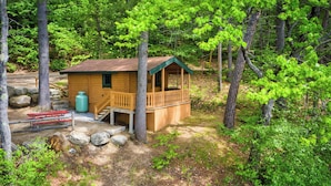 A wooden cabin with a porch, surrounded by trees and rocks.